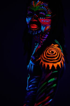 portrait of african man painted in fluorescent paint on face and shirtless muscular torso, studio shot with UV light.の写真素材