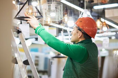 young caucasian male warehouse worker at workplace, man in green uniform and protective helmet enjoy working in big market, factoryの写真素材