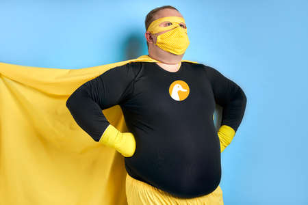 cleaning superhero saves the world from dirt, man has duck picture on costume, he is in yellow wear and in protective gloves, posing isolated over blue backgroundの写真素材