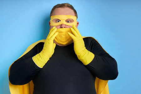 suprised caucasian superhero man in mask isolated over blue background. crazy guy in shock, wearing protective glovesの写真素材
