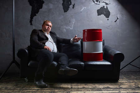 displeased caucasian male is in desperate, he sits in contemplation with oil barrel. oil industry, global market, business, petroleum, crisic conceptの写真素材