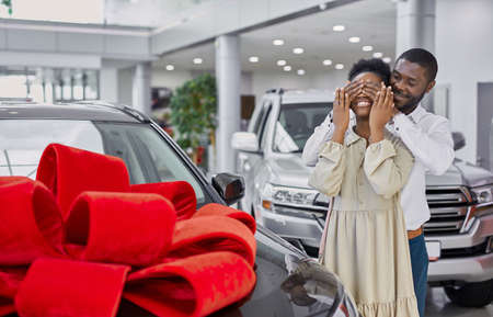 kind black man gave a car to his wife, the car is wrapped in a red bow, man closed womans eyes, prepared surpriseの写真素材