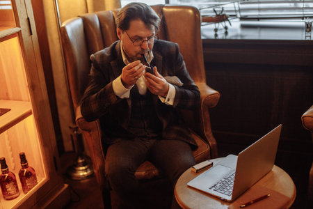 Creative male bearded mature editor pondering over new article in magazine, sitting with laptop...