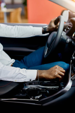 close-up photo of young black man sitting behind the wheel, trying new auto bought in cars showroom