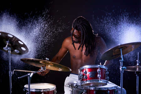 African drummer man musician hitting on wet drum cymbal and water splashing in slow motion isolated over dark backgroundの写真素材