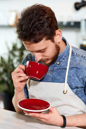 Romantic tender man with magnificent red coffee set in hands, smells aromatic fresh prepared hot...