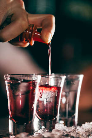 Red alcohol shots are being poured in glasses isolated on dark blurred background.Concept of Alcohol Drinks, Cocktail, Nightlife, Night Restの写真素材