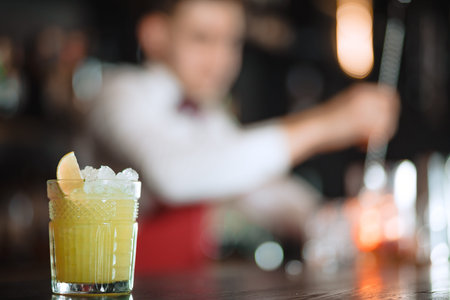 Alcohol cocktail with ice and lemon in glass isolated on blurred restaurant with barman on...