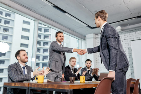 young business partners shaking hands after successful meeting, discussing business interaction,...