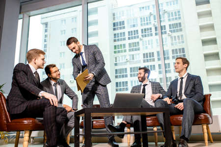 togetherness and partnership of young caucasian business men at work, group of men in tuxedo isolated in modern office, gathered to have discussion, conversationの写真素材