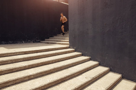 A muscular athletic man is practicing on the street staircase, doing his best. Distant view of young...