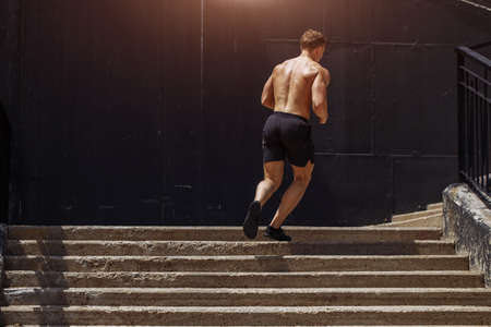 Full length of young African man in sports clothing running down the stairs while exercising outdoorsの写真素材