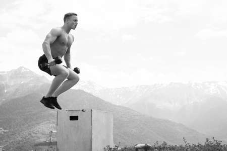 Motion shot of handsome strong man doing functional workout on sky and mountain background, performing Box jump exercise outdoor.の写真素材