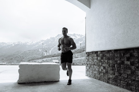 Active shirtless gogger man with muscular naked body running at daytime in countryside over...