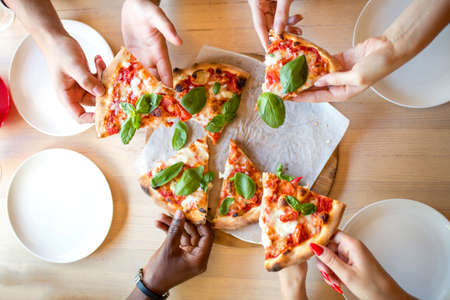 High angle shot of unrecognizable mixed race peoples hands each grabbing a slice of pizzaの写真素材