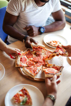 High angle shot of unrecognizable mixed race peoples hands each grabbing a slice of pizzaの写真素材