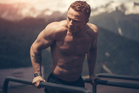 Strong crossfit sportsman with naked perfect torso doing dips on horisontal bars in outdoor...