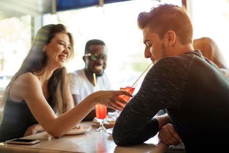 Happy multietnhic friends enjoying appetizer in american bar, cheering with tropical fruits cocktails, enjoying leisure time spending together.の写真素材