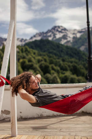 Young happy man relaxing lying in hammock on top of mountain. Summer vacation travel lifestyle conceptの写真素材