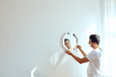 Studio portrait of young man standing near wall and hang mirror