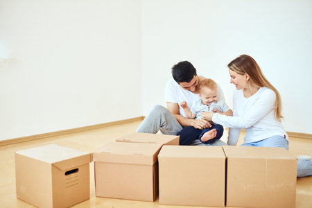 Family with little boy unpacking moving cardboard boxes at new home