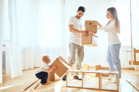 Happy family moving in new house. smiling boy help parents and carrying moving boxes on foreground