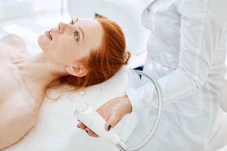 Apparatus face treatment in medical spa center, beautiful redhead lady receiving electric facial...