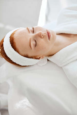 Beautician hands in disposable gloves wipe with cotton pad female client face, preparing to the cosmetological procedure. Patient lies on the couch with closed eyes in beauty salon.の写真素材