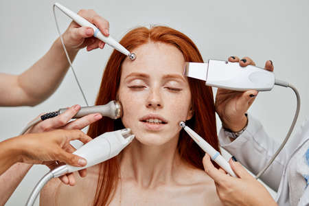 Gorgeous caucasian female with delightful emotional face enjoying modern skin care and treatment technologies. All together at the same time. Cosmetology skin care. Aesthetic facial treatment Concept.の写真素材