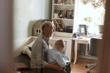 Grandfather and grandson using digital tablet for surfing internet and playing game in living roomの写真素材