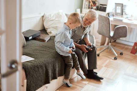 Cute little boy with grandfather sitting on sofa and playing video game with game padの写真素材
