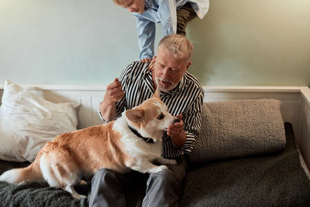 Grandfather and grandson with dog sitting at couch in living roomの写真素材