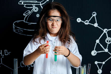 Mixed race asian little girl wearing white lab coat and protective glasses doing plain experiments in elementary science labの写真素材