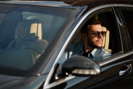 pensive attractive man looking aside while sitting in the car. close up side view photo. driving...