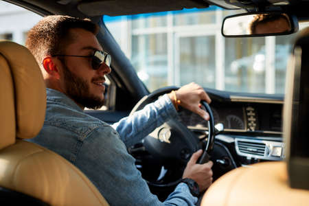 sporty brutsl man in sunglasses is looking at the traffic light while driving . back view photoの写真素材