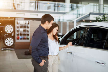Successful caucasian busuinessman in formal wear and his elegant young wife examining a new car in motor show.の写真素材