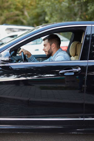 black-haired bearded guy is sitting on his new car. close up side view photo. free time, taxi conceptの写真素材