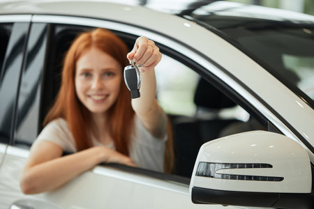 Ready to get on the road. Attractive young red haired woman sitting at the front seat of the car...