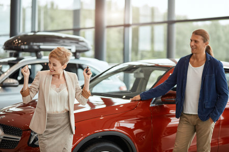 Female sales manager standing at the dealership telling about the features of the car to the...