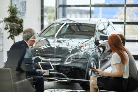 Portrait of two car buyers reading sale contract and signing a car insurance policy papers to buy a car with a car loan in the showroom.の写真素材