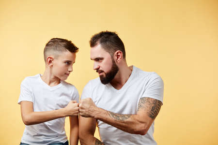 father and son look seriously at each other, keeps fists together, ready to fight on yellowの写真素材