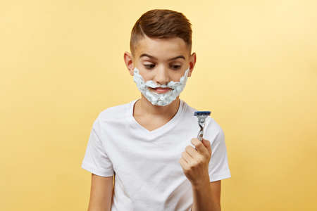 shocking boy do not know how shaving with razor blade in his hand, on yellow backgroundの写真素材