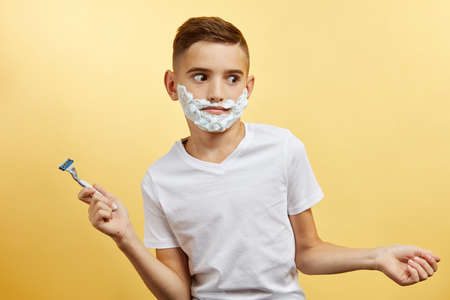 shoking boy do not know how shaving with razor blade in his hand, on yellow backgroundの写真素材