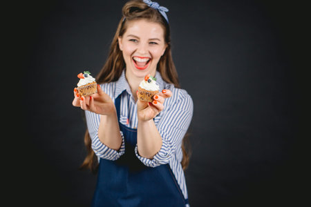 Happy young bakery woman holding cupcakes in hands, offering to taste