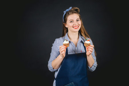 Pretty young housewife holding cupcakes in hands pleasently smiling, ready to eat