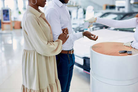 staff of dealership is checking temperature of clients, african couple came to buy auto, but before it they need to be examined for covid-19, coronavirus epidemicの写真素材