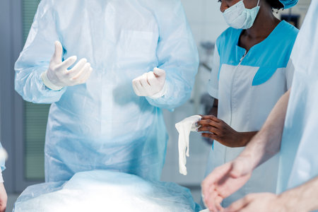 beautiful african doctor puts on medical gloves before operation, close up cropped photo.