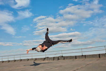 Street dancer hipster guy makes back flip with arm support. Asian Breakdancer exercising on roof. Low angle mid-air view against blue sky backgroundの写真素材