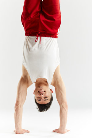 Chinese break dancer in red sweatpants showing his skills on white background, performing a...
