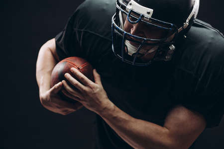 American football player with helmet and armour passing a ball while running on field at nightの写真素材